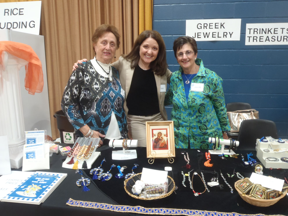 Parishioners smiling at a festival table displaying Greek jewelry
